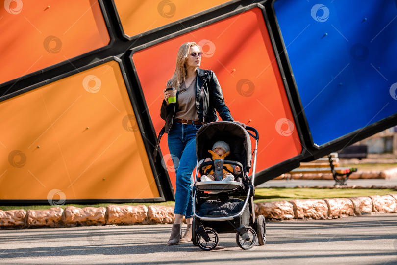 Скачать Молодая красивая мама гуляет по парку с малышом в коляске, пьет кофе фотосток Ozero