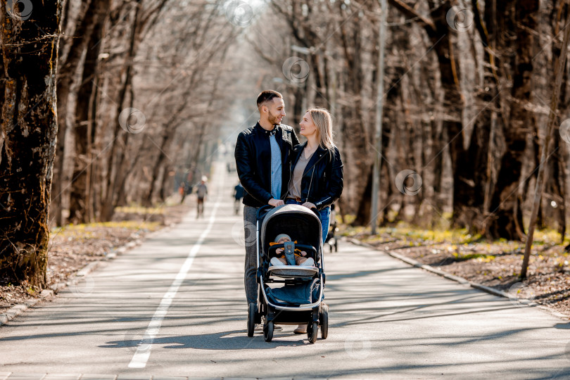 Скачать молодая семья прогуливается весной по парку с малышом в коляске. Счастливые родители фотосток Ozero