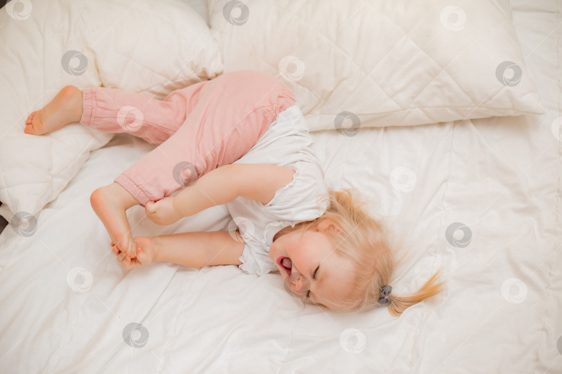 Скачать Симпатичная маленькая блондинка лежит дома в постели с белым постельным бельем, вид сверху фотосток Ozero