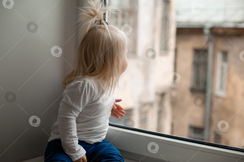 Скачать Маленькая девочка сидит на подоконнике дома и смотрит в окно фотосток Ozero