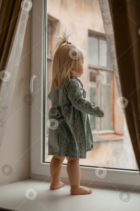 Скачать Симпатичная малышка-блондинка в винтажном платье стоит у окна дома фотосток Ozero