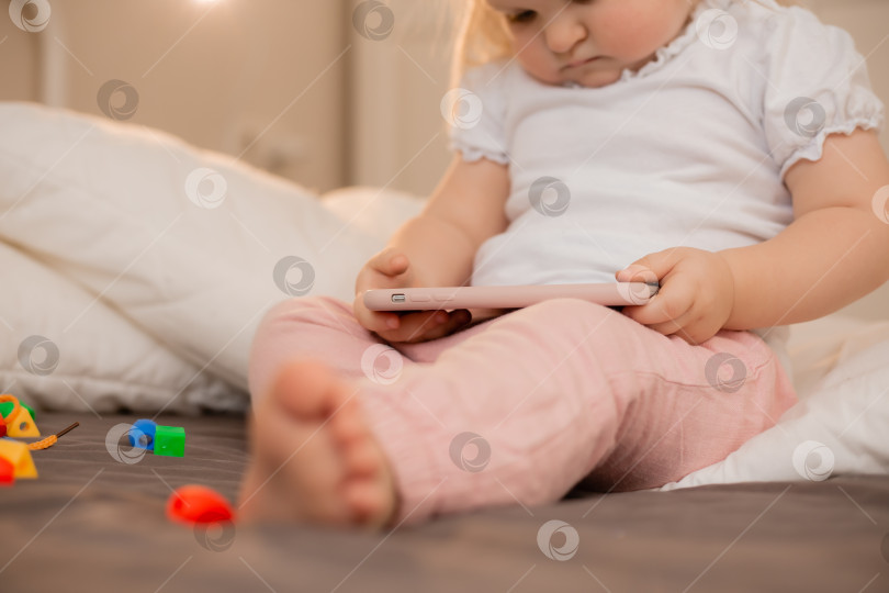 Скачать Малышка блондинка играет с телефоном дома на кровати. Дети и технологии фотосток Ozero