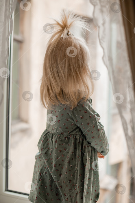 Скачать Симпатичная малышка-блондинка в винтажном платье стоит у окна дома фотосток Ozero