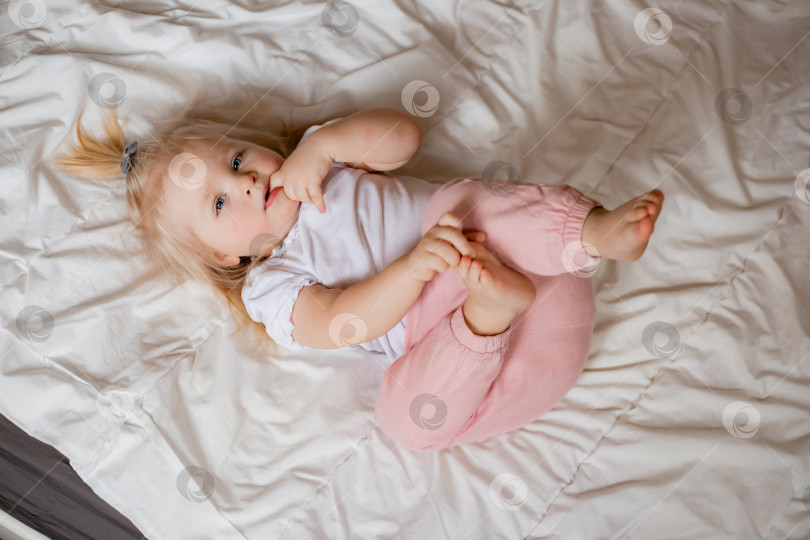Скачать Симпатичная маленькая блондинка лежит дома в постели с белым постельным бельем, вид сверху фотосток Ozero