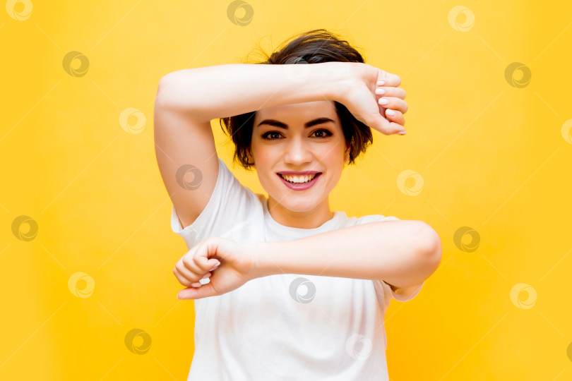 Скачать Молодая счастливая брюнетка с короткой стрижкой в белой футболке на желтом фоне. портрет молодой женщины с различными эмоциями на желтом фоне. пространство для текста фотосток Ozero