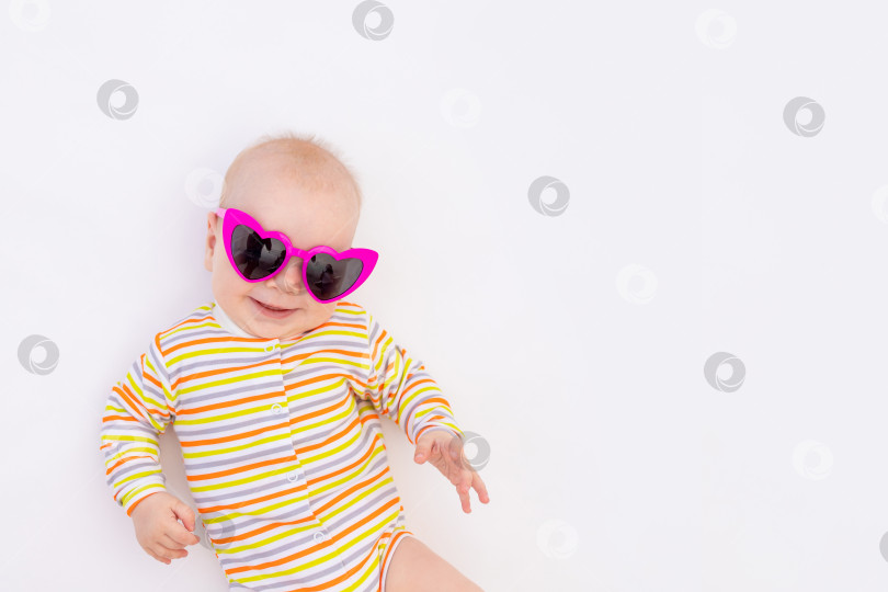 Скачать маленькая улыбающаяся девочка 6 месяцев, лежащая на белом изолированном фоне в ярких солнцезащитных очках, место для текста фотосток Ozero