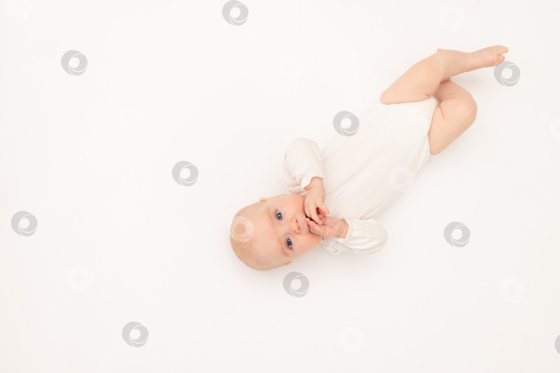 Скачать симпатичная малышка в белом боди на белом изолированном фоне смотрит в камеру, малыш 3 месяцев от роду лежит на кровати, место для текста фотосток Ozero