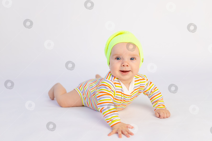 Скачать маленькая улыбающаяся девочка 6 месяцев лежит на белом изолированном фоне в ярком боди и желтой шапочке, место для текста фотосток Ozero