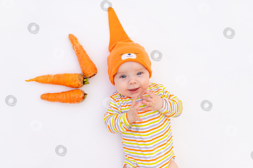 Скачать маленькая девочка 6 месяцев, лежащая на белом изолированном фоне с морковкой, место для текста, первый прикорм, концепция детского питания фотосток Ozero
