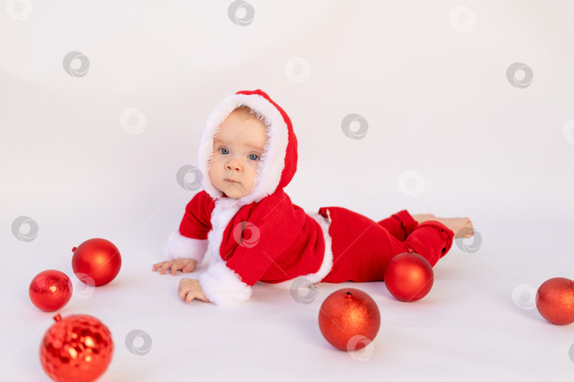 Скачать маленький ребенок лежит в костюме Санты на белом изолированном фоне с красными рождественскими шарами, место для текста, рождественская концепция фотосток Ozero
