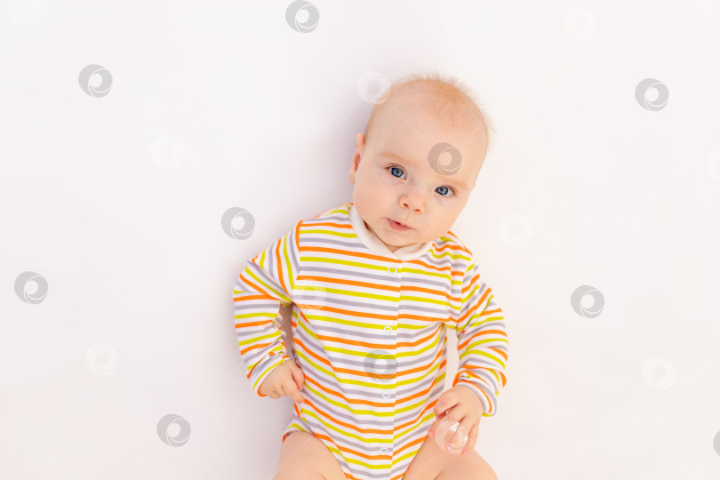 Скачать улыбающаяся девочка 6 месяцев, лежащая на белом изолированном фоне в ярком боди, место для текста, вид сверху. Здоровый счастливый ребенок. фотосток Ozero