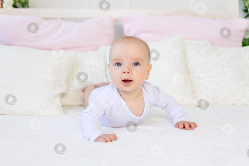 Скачать малышка 6 месяцев в белом боди лежит на животе на белой кровати дома фотосток Ozero