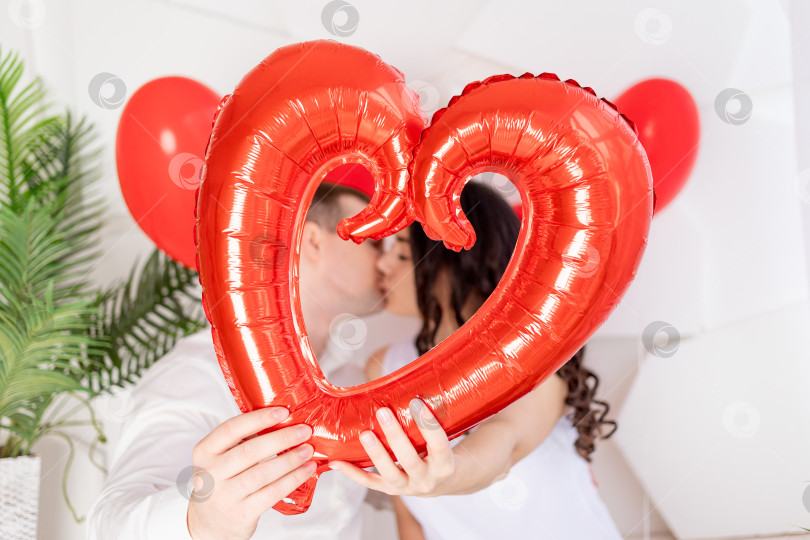 Скачать влюбленная пара поздравляет друг друга с Днем Святого Валентина, обнимаясь и целуясь, держа в руках большое красное сердце фотосток Ozero