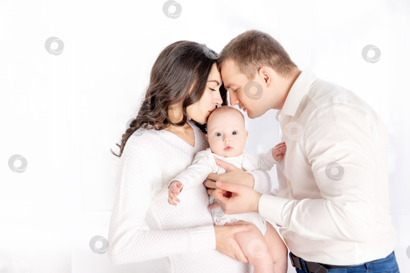 Скачать мама и папа целуют новорожденного ребенка, держа его на руках дома у окна, концепция счастливой любящей семьи, стиль жизни фотосток Ozero