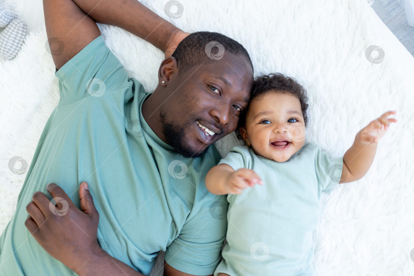 Скачать счастливый улыбающийся афроамериканский папа с маленьким сыном на кровати дома в обнимку, счастливая семья, день отца фотосток Ozero