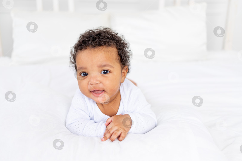 Скачать симпатичный афроамериканский малыш лежит на белой кровати в спальне дома фотосток Ozero