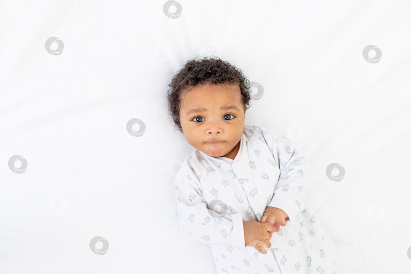 Скачать Афроамериканский малыш лежит в пижаме на белой кровати в спальне фотосток Ozero