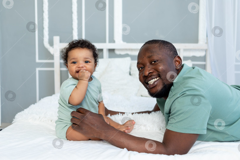 Скачать счастливый улыбающийся афроамериканский папа с маленьким сыном дома на кровати, обнимаются и играют, счастливая семья, день отца фотосток Ozero