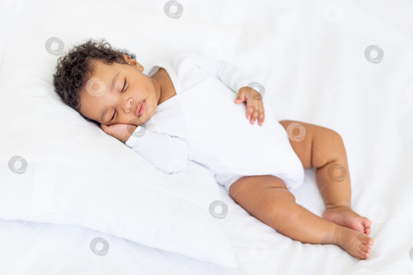 Скачать Маленькая афроамериканка спит дома на белой кровати, подложив ладошку под щеку фотосток Ozero