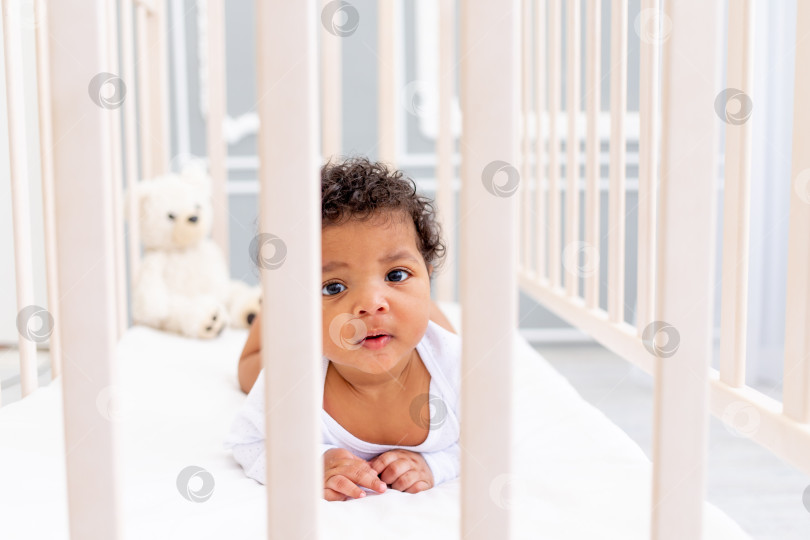Скачать симпатичный афроамериканский малыш в белой кроватке для сна выглядывает из-за бортика фотосток Ozero