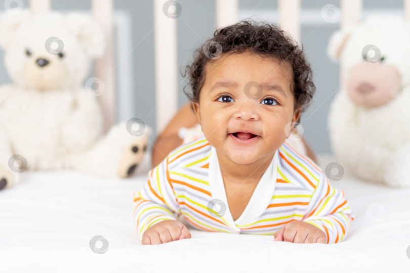 Скачать счастливый и улыбающийся маленький афроамериканец в кроватке с игрушками фотосток Ozero