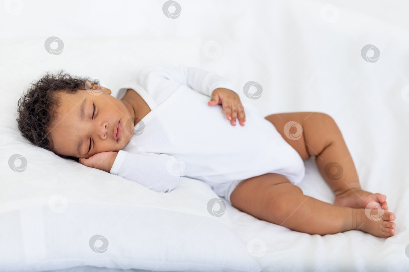Скачать Маленькая афроамериканка спит дома на белой кровати, подложив ладошку под щеку фотосток Ozero