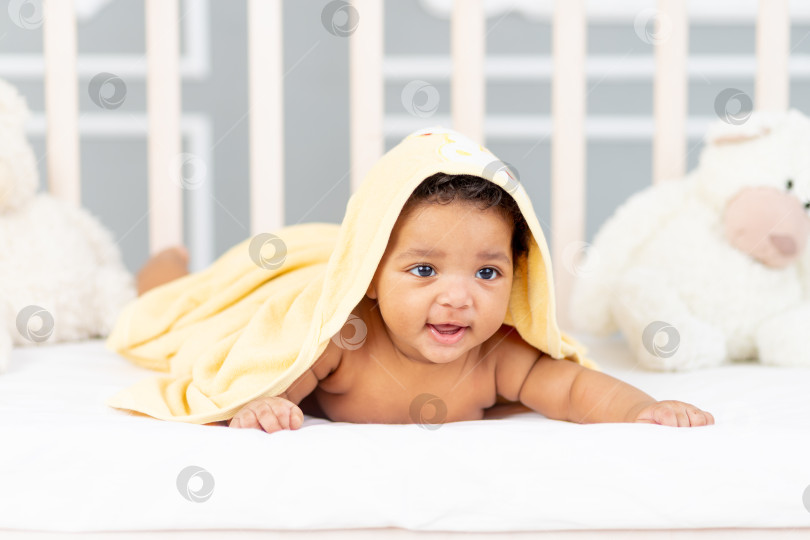 Скачать Улыбающийся маленький ребенок-афроамериканец лежит в кроватке после купания в желтом полотенце фотосток Ozero