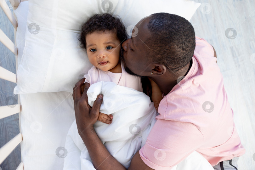 Скачать афроамериканский папа целует и обнимает маленького сына в кроватке перед тем, как лечь спать фотосток Ozero