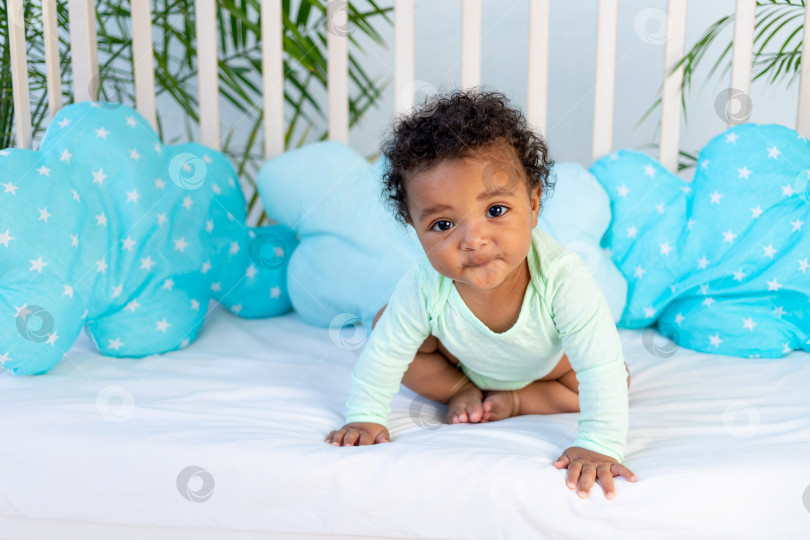 Скачать милый африканский малыш сидит дома в кроватке перед отходом ко сну на голубой кровати, концепция здорового сна и хлопковые аксессуары для детского постельного белья фотосток Ozero