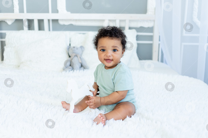 Скачать симпатичный афроамериканский малыш играет с деревянной лошадкой дома на кровати в спальне и улыбается фотосток Ozero