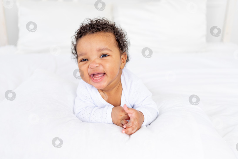 Скачать улыбающийся афроамериканский малыш на белой кровати в спальне смеется фотосток Ozero