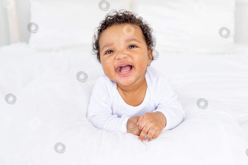 Скачать улыбающийся афроамериканский малыш на белой кровати в спальне смеется фотосток Ozero
