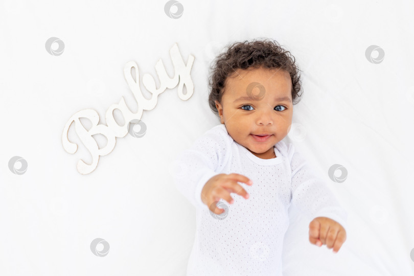 Скачать Маленький ребенок-афроамериканец лежит на белой кровати и улыбается фотосток Ozero