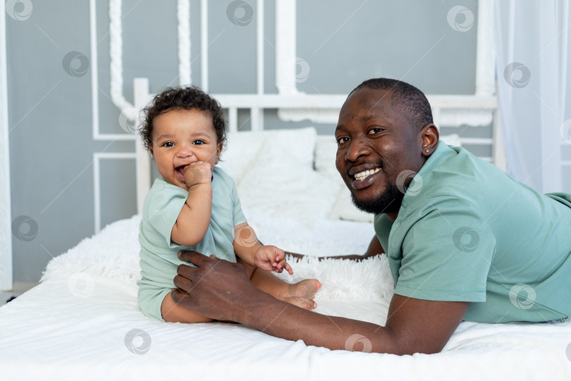 Скачать счастливый улыбающийся афроамериканский папа с маленьким сыном дома на кровати, обнимаются и играют, счастливая семья, день отца фотосток Ozero