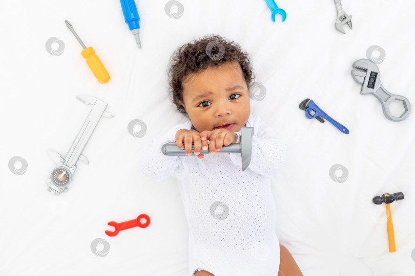 Скачать Афроамериканский маленький ребенок со строительными инструментами, лежащий на белой кровати, концепция строительства и ремонта фотосток Ozero