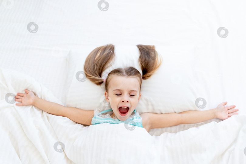 Скачать маленькая девочка проснулась утром дома на кровати, застеленной белым хлопком, и зевает во весь рот фотосток Ozero