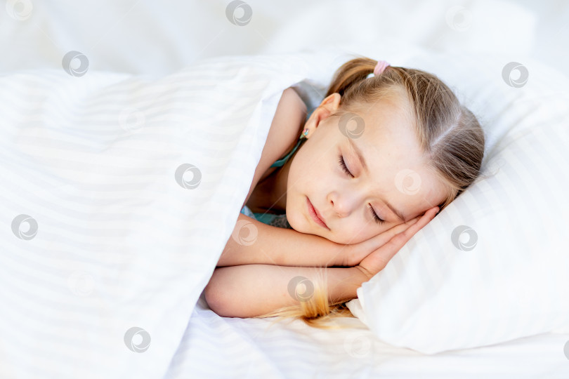 Скачать девочка спит дома на кровати, застеленной белым хлопком, и сладко улыбается во сне, подложив ладошки под щеки фотосток Ozero