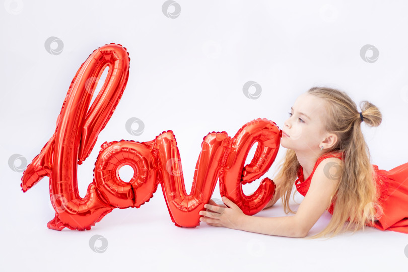 Скачать маленькая девочка в красном платье держит большой воздушный шар с надписью Love на белом изолированном фоне, концепция дня Святого Валентина, место для текста фотосток Ozero