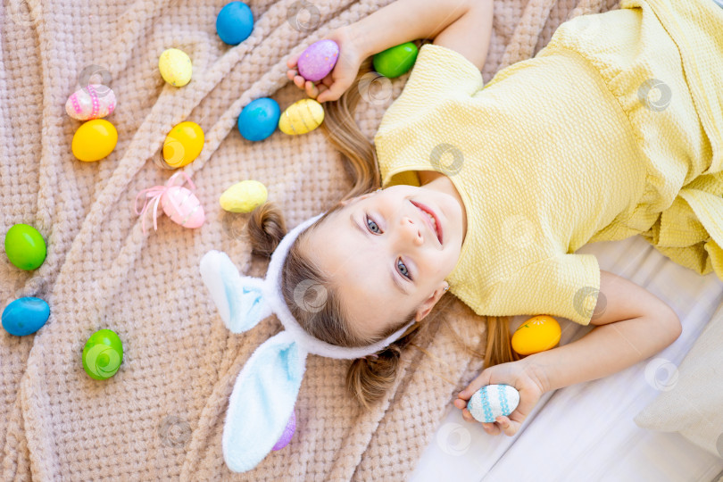 Скачать пасха, маленькая девочка среди раскрашенных крашеных яиц готовится к празднику, улыбается и веселится, вид сверху фотосток Ozero