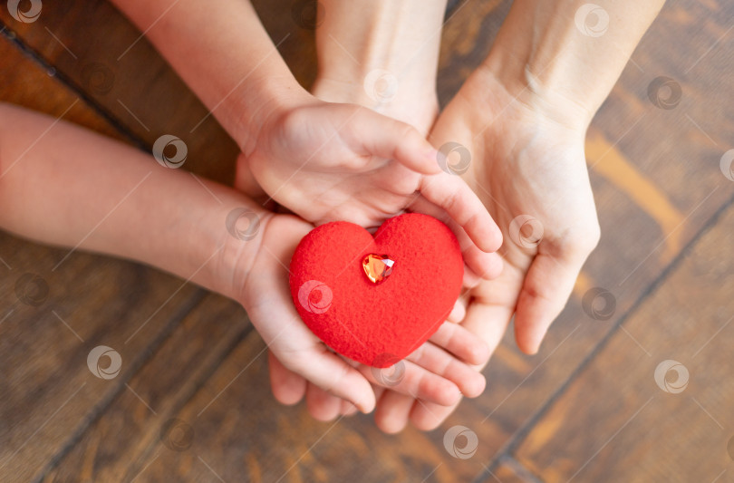 Скачать мамины руки держат руки ребенка, а внутри красное сердечко на деревянном коричневом фоне - концепция Дня святого Валентина или дня матери фотосток Ozero