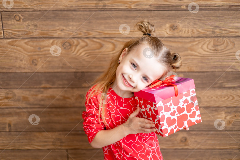 Скачать маленькая счастливая девочка в красной пижаме с большим подарком в руках на темно-коричневом деревянном фоне смеется и улыбается, концепция дня святого Валентина, место для текста фотосток Ozero