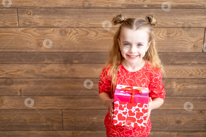 Скачать маленькая счастливая девочка в красной пижаме с большим подарком в руках на темно-коричневом деревянном фоне смеется и улыбается, концепция дня святого Валентина, место для текста фотосток Ozero