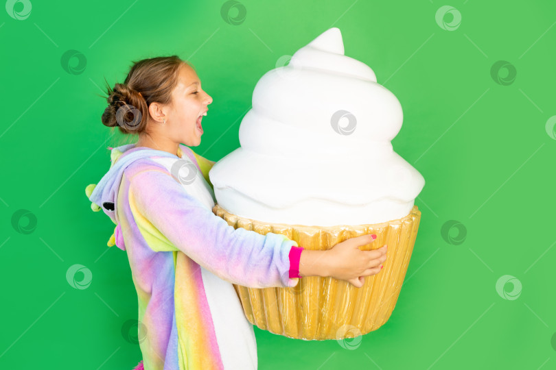 Скачать маленькая девочка на зеленом фоне в ярком костюме держит в руках огромный торт. Место для текста. Концепция нездоровой пищи и похудения фотосток Ozero