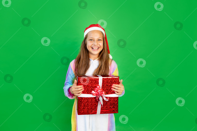 Скачать симпатичная маленькая девочка на зеленом изолированном фоне в ярком костюме и шапке Санты с подарком в руках. Место для текста. Концепция Нового года и Рождества фотосток Ozero