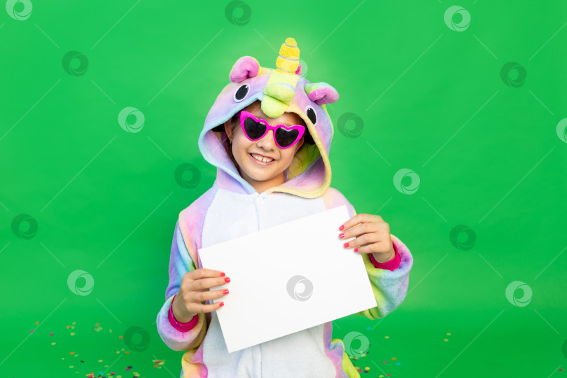 Скачать маленькая девочка на зеленом фоне в ярком костюме, держащая в руках белый лист бумаги. Место для текста. Концепция праздника, Дня рождения и распродаж фотосток Ozero