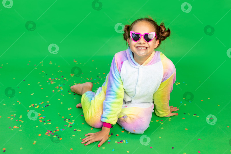 Скачать маленькая девочка сидит на зеленом изолированном фоне с серпантином в ярком костюме и очках. Место для текста. Концепция праздника, Дня рождения и распродаж фотосток Ozero