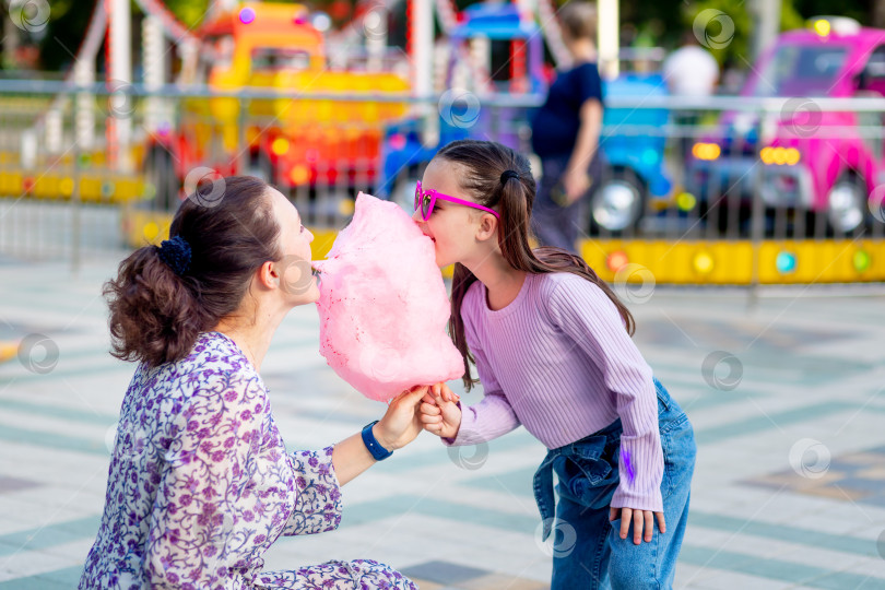 Скачать маленькая девочка со своей мамой летом в парке развлечений едят сахарную вату и мороженое возле каруселей, дурачатся и смеются - концепция семейных выходных и школьных каникул фотосток Ozero