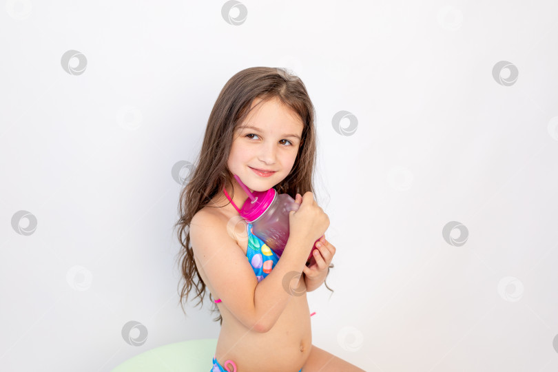 Скачать маленькая девочка 5-6 лет сидит в купальнике с коктейлем на белом изолированном фоне, место для текста фотосток Ozero