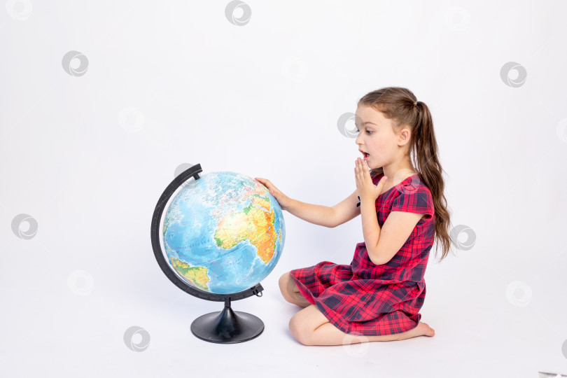 Скачать 7-летняя школьница сидит в красном платье с глобусом на белом изолированном фоне, место для текста, 1 сентября, День знаний фотосток Ozero