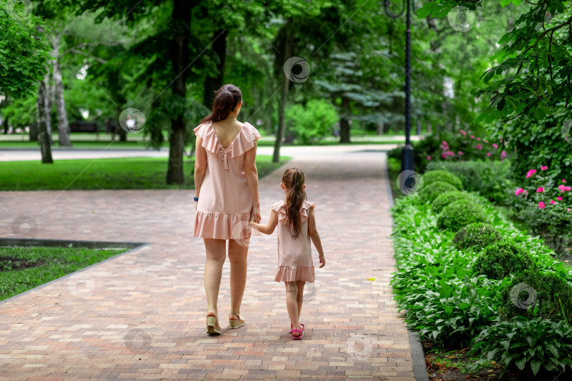 Скачать Счастливые мать и дочь 5-6 лет гуляют летом в парке, держась за руки, концепция счастливой семьи. вид сзади фотосток Ozero